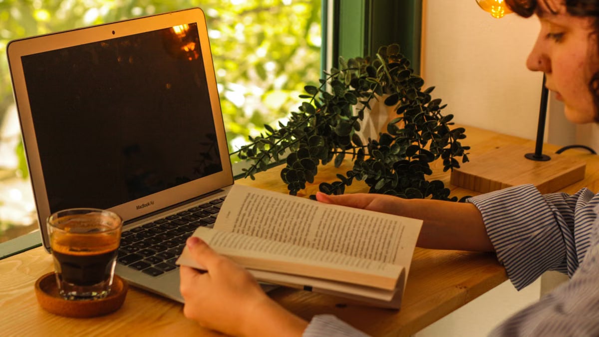 Warm indoor setting with a laptop, coffee, and book creating a cozy workspace.